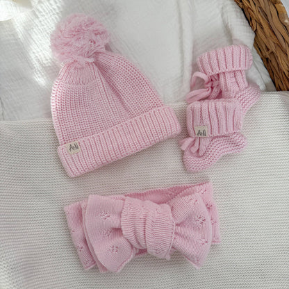 Pink knitted beanie, pink booties, and matching bow accessory set on fabric