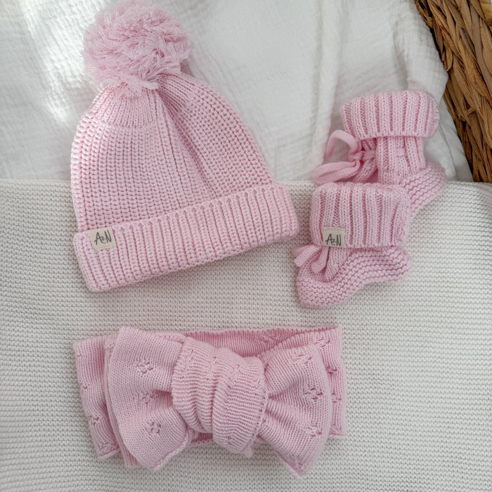 Pink knitted beanie with pom-pom, pink knitted booties, and matching bow set
