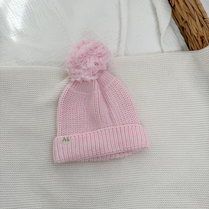 Pink knitted baby hat with fluffy pom-pom and ribbed brim