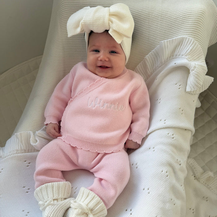 Baby wearing pink kimono set with ruffled collar and matching pants, cream bow headband