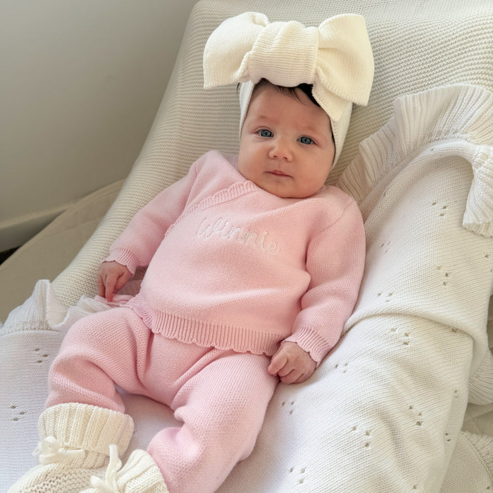 Newborn in pink kimono set with embroidered text, ruffle hem, and cream bow hair accessory