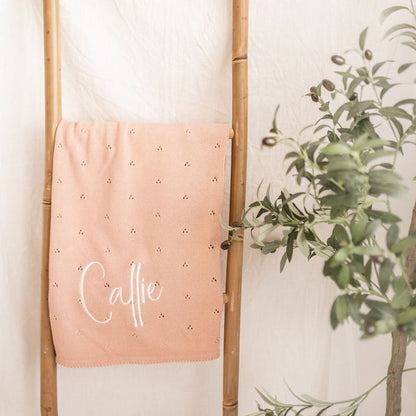 Personalized baby knit blanket draped on stand, pink pointelle with 'Calle'