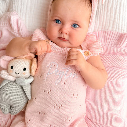 Pink pointelle romper close-up with knit texture, button straps, and personalized print
