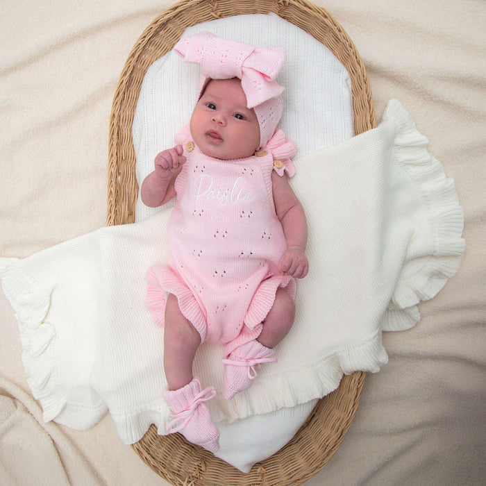 Pink pointelle summer romper with bow straps and ruffled legs on a baby