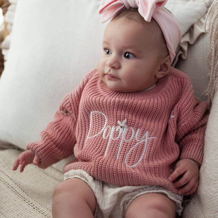 Pink knitted baby jumper with cursive 'Poppy' lettering across the chest