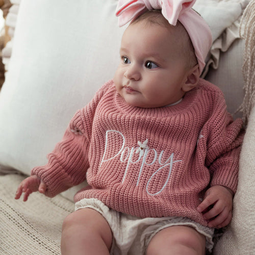 Pink knitted baby jumper with cursive 'Poppy' lettering across the chest