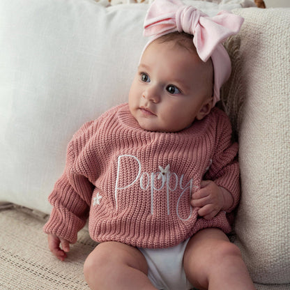 Pink knitted baby jumper with cursive 'Poppy' on the front, long sleeves