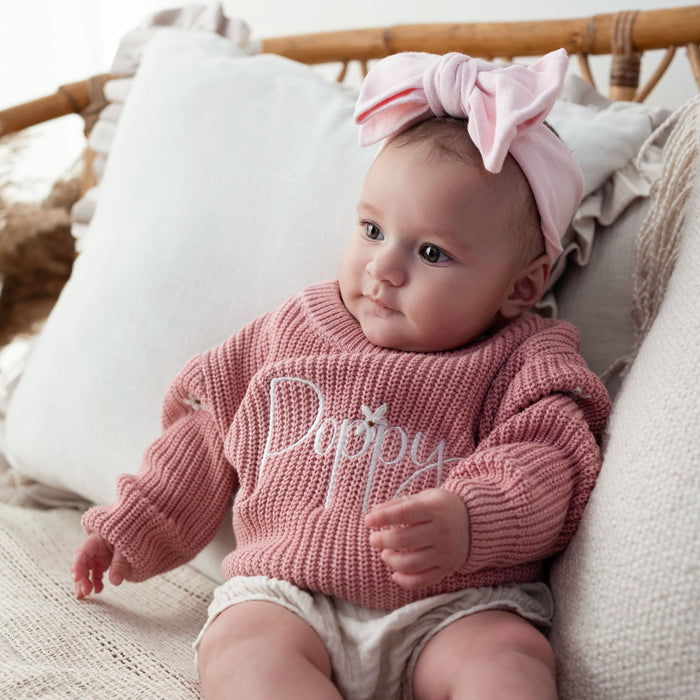 Pink knit baby jumper with 'Poppy' script on the chest and ribbed cuffs