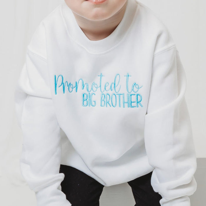 White sweatshirt close-up with 'Promoted to BIG BROTHER' blue printed lettering