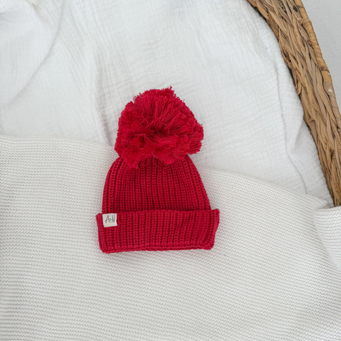 Red knit pom-pom beanie with ribbed cuff and woven label patch