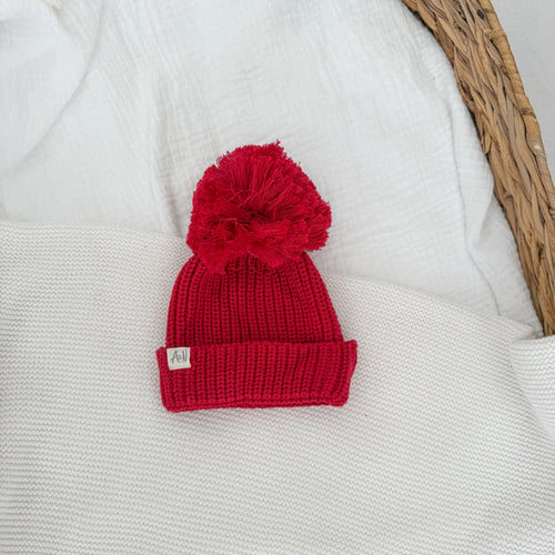 Red knit pom-pom beanie with ribbed cuff and woven label patch