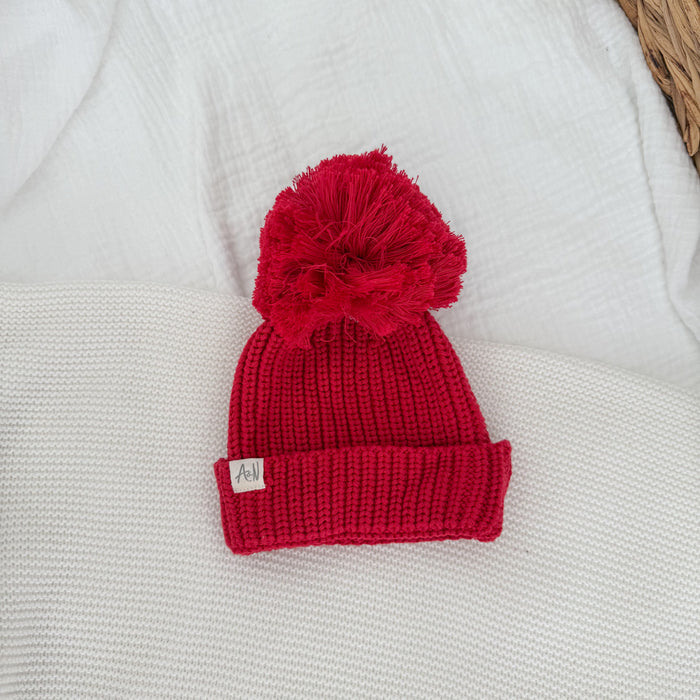 Red knit beanie hat with pom-pom and ribbed fold-up cuff, small label patch