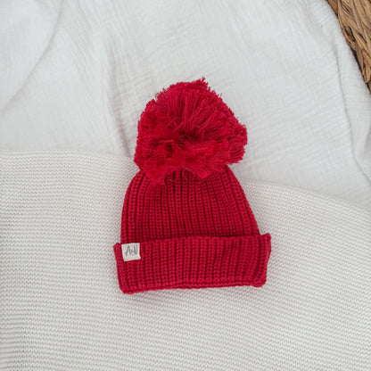 Red knit beanie hat with pom-pom and ribbed fold-up cuff, small label patch