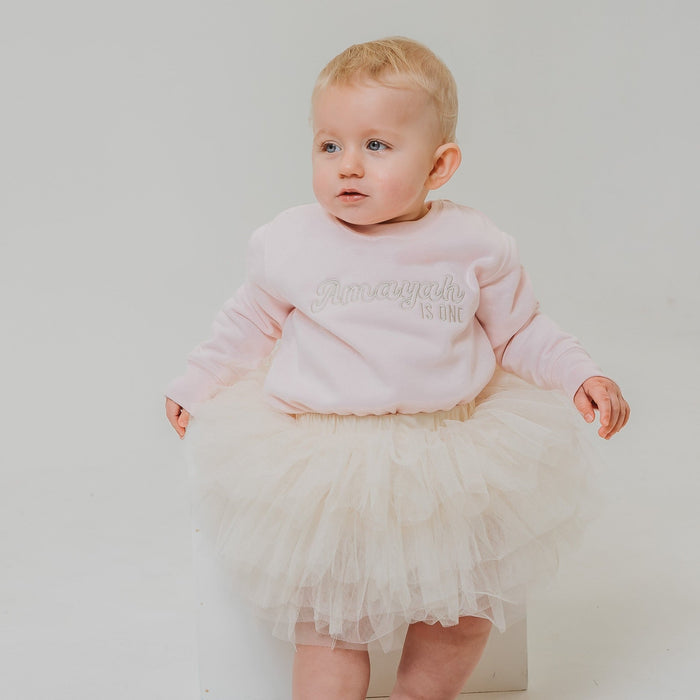 Light pink baby sweatshirt with hood and glitter 'is one' print at chest