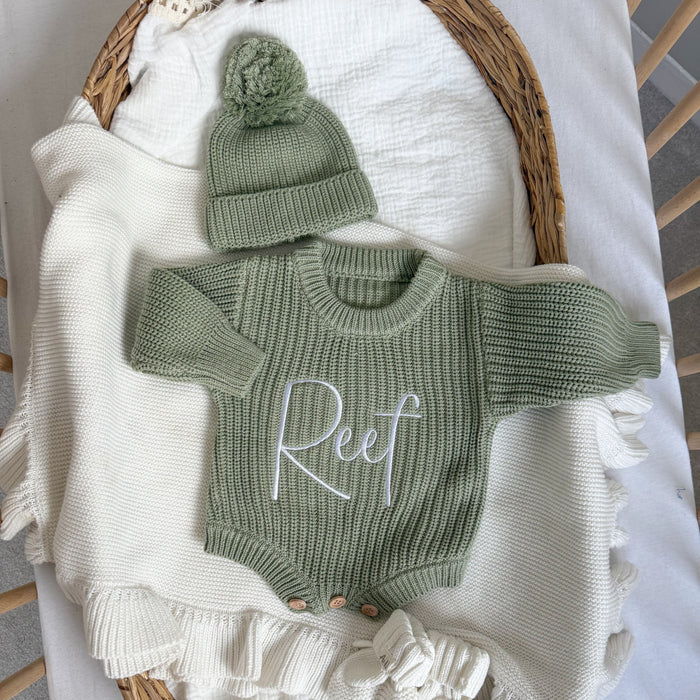 Sage green knitted romper with embroidered name, ribbed cuffs, and matching beanie