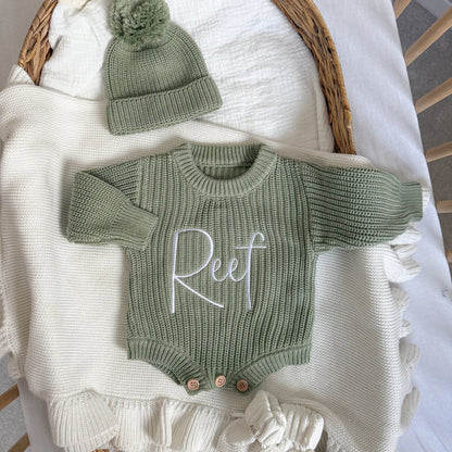 Sage green knitted romper with long sleeves, embroidered name, and buttoned shorts hem