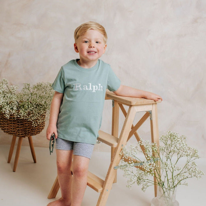 Sage green personalized T-shirt with 'Ralph' front print, child standing