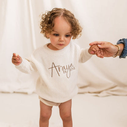 White knitted baby jumper with long sleeves and script 'is ONE' on chest