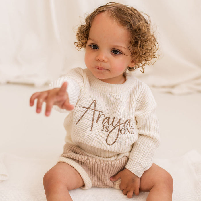 White knitted baby jumper with long sleeves and 'is ONE' script front print