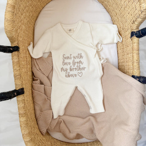 Cream knitted baby romper with embroidered message and tan contrast panels, snap buttons