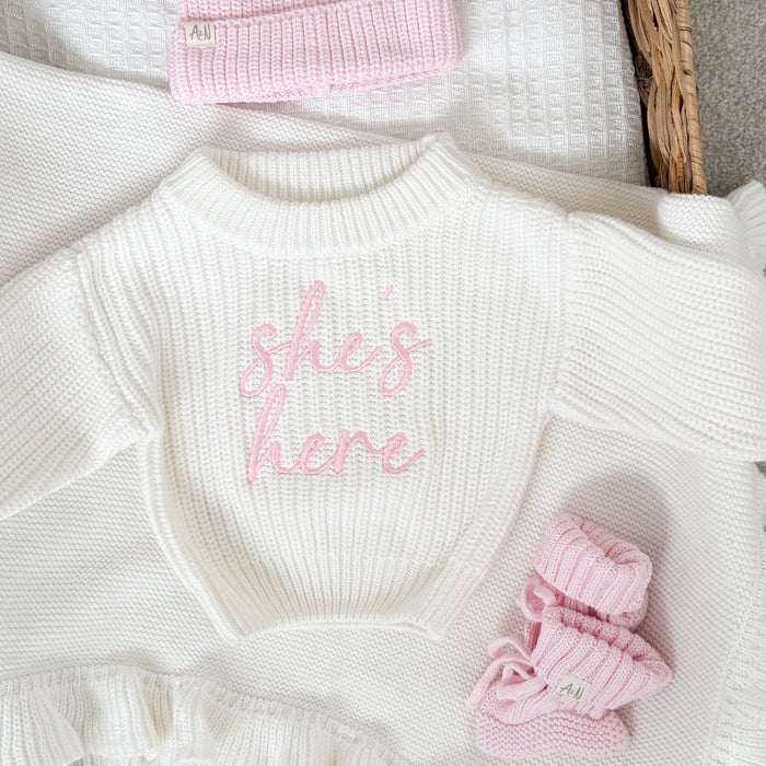 White knitted jumper close-up: pink script logo, ribbed crew neck, textured knit