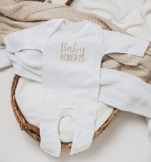White embroidered baby romper with script "Baby ROBERTS" on front