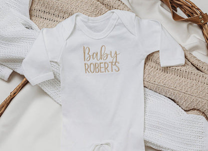 White embroidered baby romper with script "Baby ROBERTS" chest detail