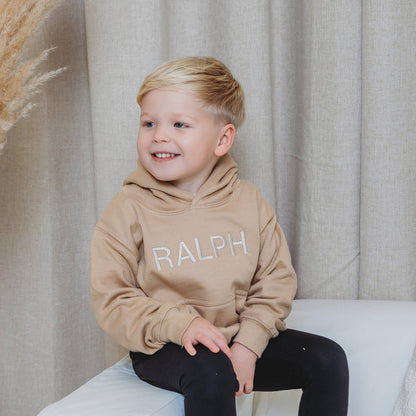 Tan kids embroidered hoody with bold RALPH lettering, smiling side view