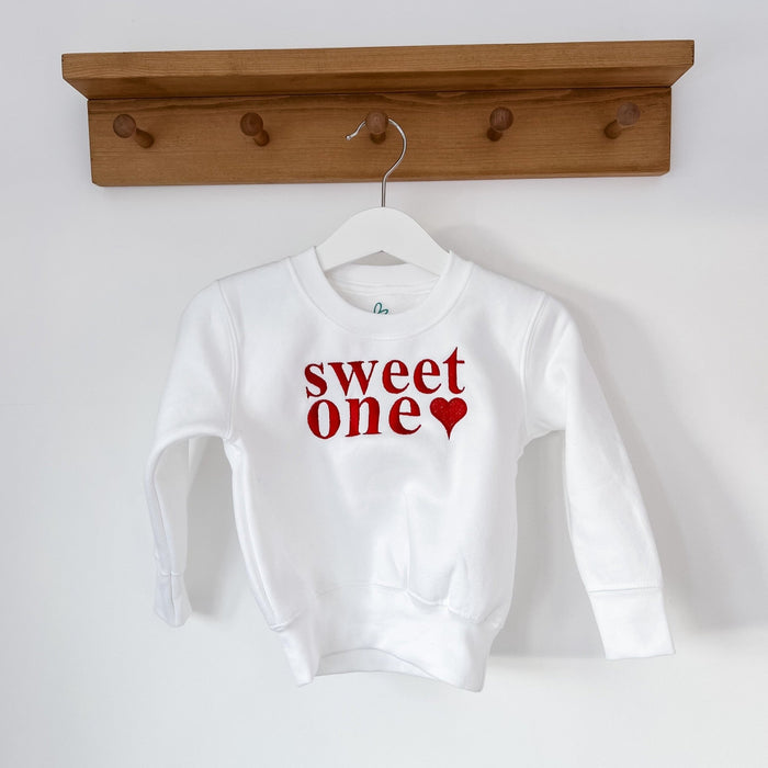 White sweatshirt on hanger with 'sweet one' red lettering and small heart
