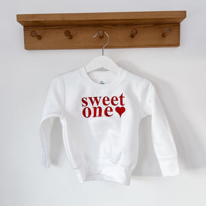 White sweatshirt on hanger with 'sweet one' red lettering and small heart