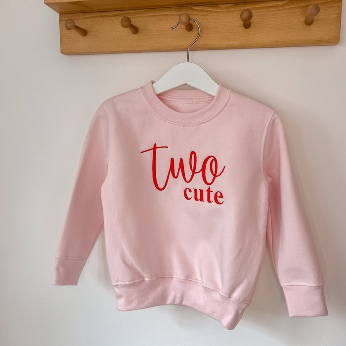 Pink pullover sweatshirt with red 'Two cute' graphic on chest, crew neck