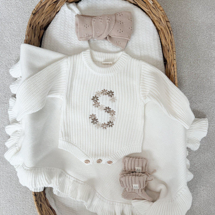 White knitted baby romper with embroidered floral letter, ruffled hem, and bow detail