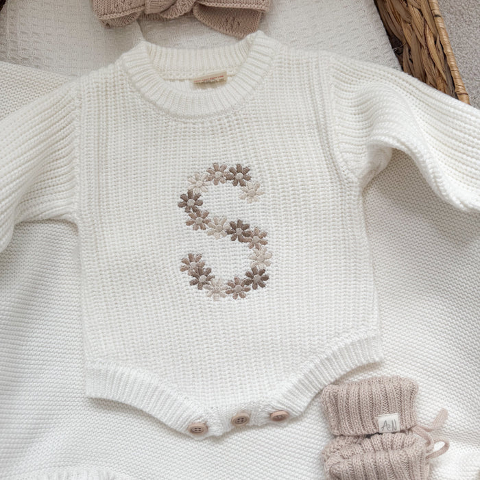 White knitted baby romper close-up with embroidered floral letter and snap-button placket