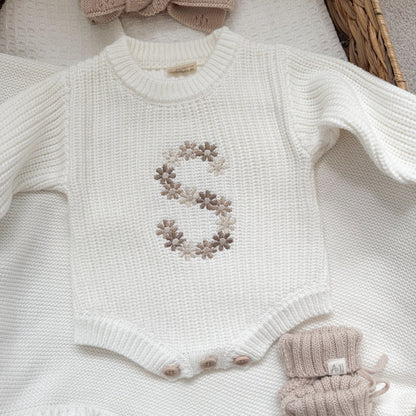 White knitted baby romper close-up with embroidered floral letter and snap-button placket
