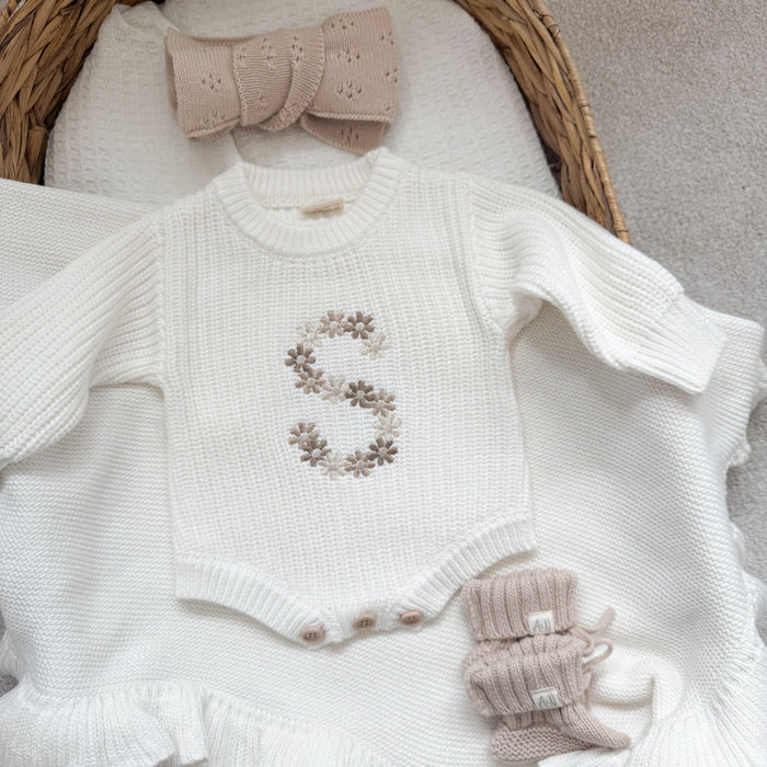 White knitted baby romper with embroidered floral letter and ruffle hem detail