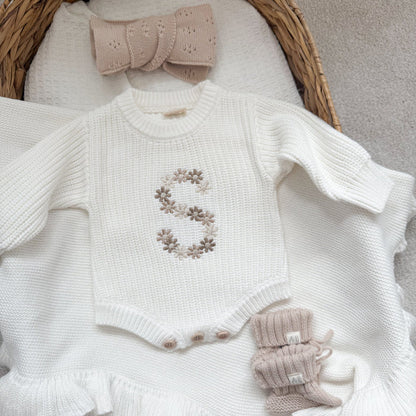 White knitted baby romper with embroidered floral letter and ruffle hem detail