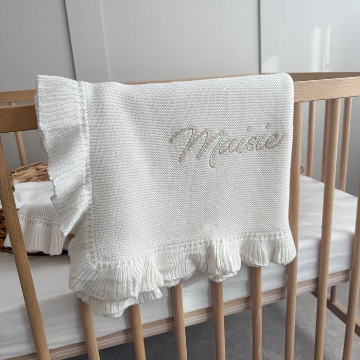 White knitted blanket with ruffled frill trim and embroidered name in script