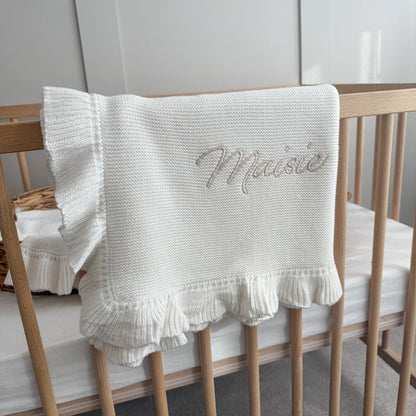 White knitted blanket with ruffled frill trim and embroidered name in script