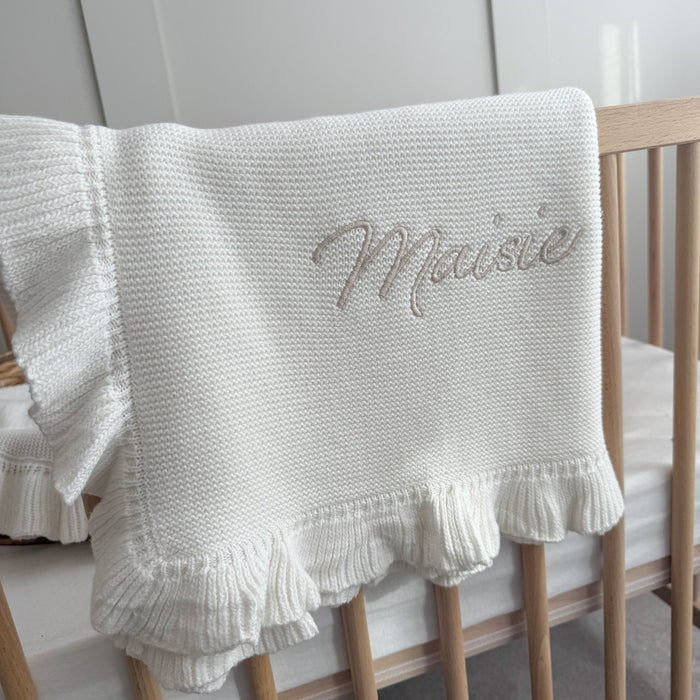White knitted blanket with frill hem and embroidered script name on center