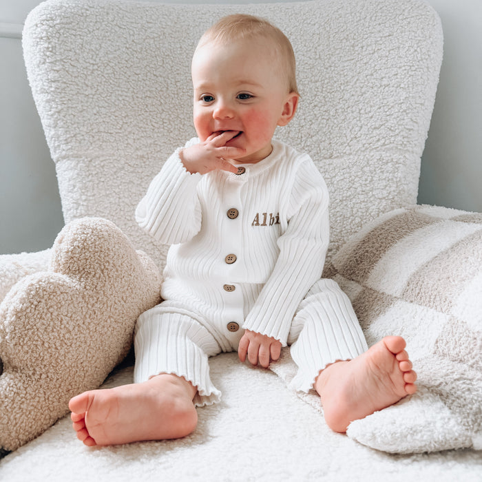 White long-sleeve knit romper with button front and embroidered name detail