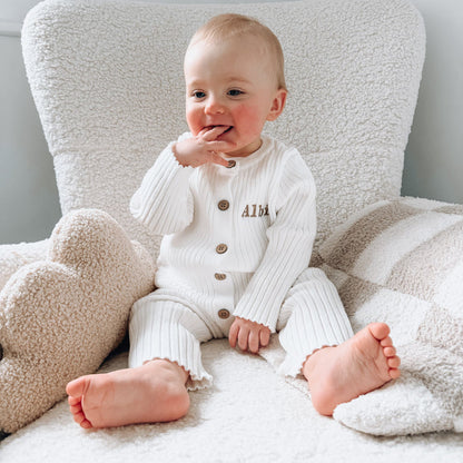 White long-sleeve knit romper with button front and embroidered name detail