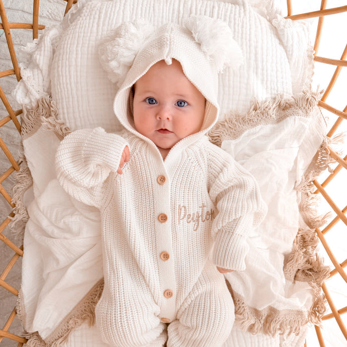 White knit pom pom romper with hood, long sleeves, and wooden-look button front