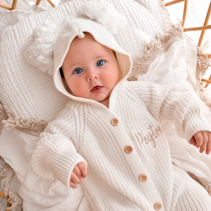 White knit hooded pom romper with long sleeves, button front, and name embroidery on chest
