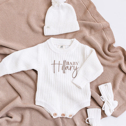 White knitted baby romper with "Baby" name print, long sleeves, and snap buttons