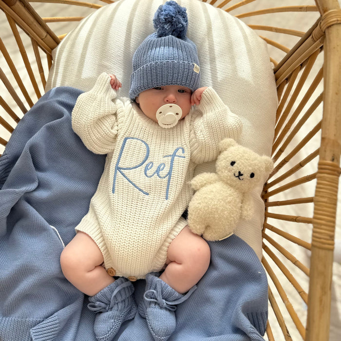 Cream knitted romper with blue 'Reef' print, blue knit hat, and plush rabbit