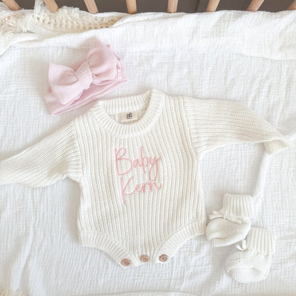 White knitted baby romper with pink name print, cuffed sleeves and snap buttons