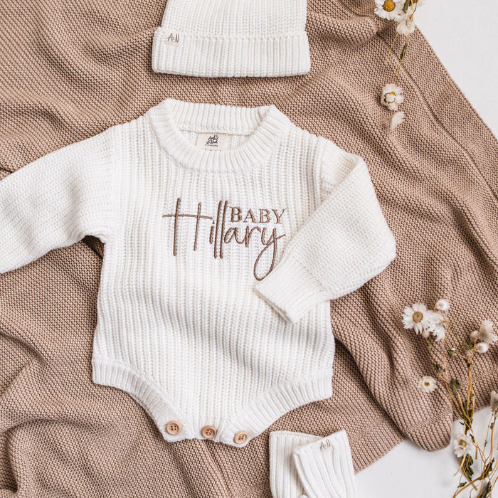 White knitted baby romper with embroidered "Baby" name, long sleeves and snap buttons