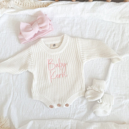 White knitted baby romper with pink "Baby" text, bow accents and snap buttons