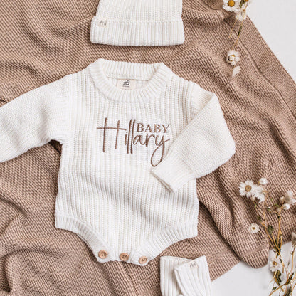 White knitted baby romper with embroidered "Baby" name, long sleeves and snap buttons
