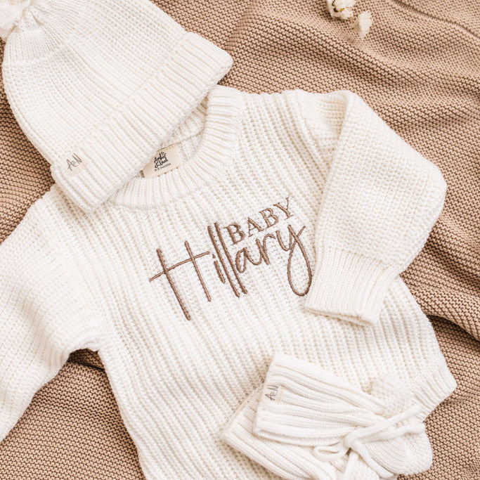 White knitted baby romper with embroidered "Baby" name and snap buttons
